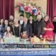 Foto perayaan ulang tahun ke-75 Ps Max Meiruntu bersama keluarga besar dan jemaat GPdI Australia yang berlangsung di Hall GPdI Sydney, Australia. Terlihat Ps Max Meiruntu berdiri di tengah mengenakan jas hitam dan dasi formal, didampingi istri dan anak-cucu serta para jemaat yang mengenakan pakaian kasual rapi dan berwarna cerah. Meja depan dihiasi dengan dekorasi kue ulang tahun, termasuk kue dengan topper bertuliskan "Happy 75 B’Day", serta dekorasi ulang tahun warna-warni seperti topi kerucut, lilin, dan tulisan "happy birthday" yang dicetak berulang kali pada banner hitam dengan font putih dan aksen warna neon. Background panggung menampilkan tirai merah marun dan dekorasi bunga segar bernuansa merah muda, biru, dan putih. Gambar ini mencerminkan suasana kekeluargaan dan sukacita dalam merayakan dedikasi panjang Ps Max Meiruntu sebagai pemimpin spiritual GPdI Australia, khususnya di GPdI Sydney selama lebih dari 35 tahun.